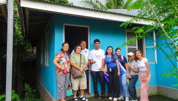 Image shows families stood outside of a house.